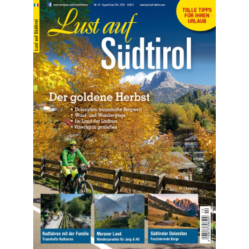 Herbstliche Landschaft mit gelb gefärbten Bäumen, Radfahrer auf Weg, Berggipfel im Hintergrund, Dorf St. Christina sichtbar.