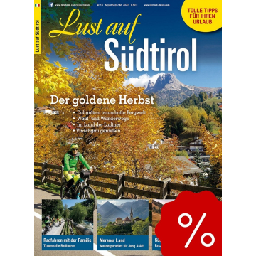 Herbstliche Landschaft mit gelb gefärbten Bäumen, Radfahrer auf Weg, Berggipfel im Hintergrund, Dorf St. Christina sichtbar.