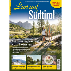 Zwei Wanderer auf Holzsteg in sonniger Berglandschaft der Dolomitenregion Kronplatz, umgeben von Tannen und Bergen